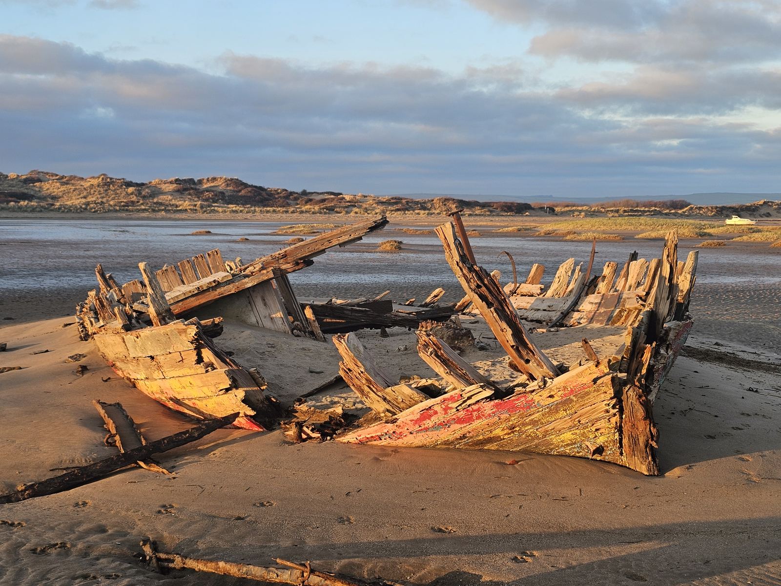 An old wreck exposed on the sand at low tide, dunes in the background