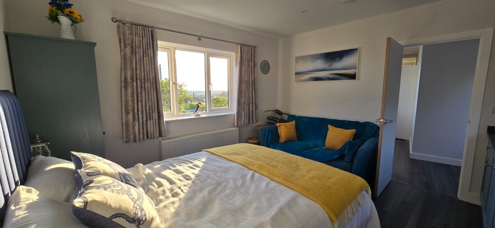 The room, with a double bed, teal sofa and a window looking out over the countryside
